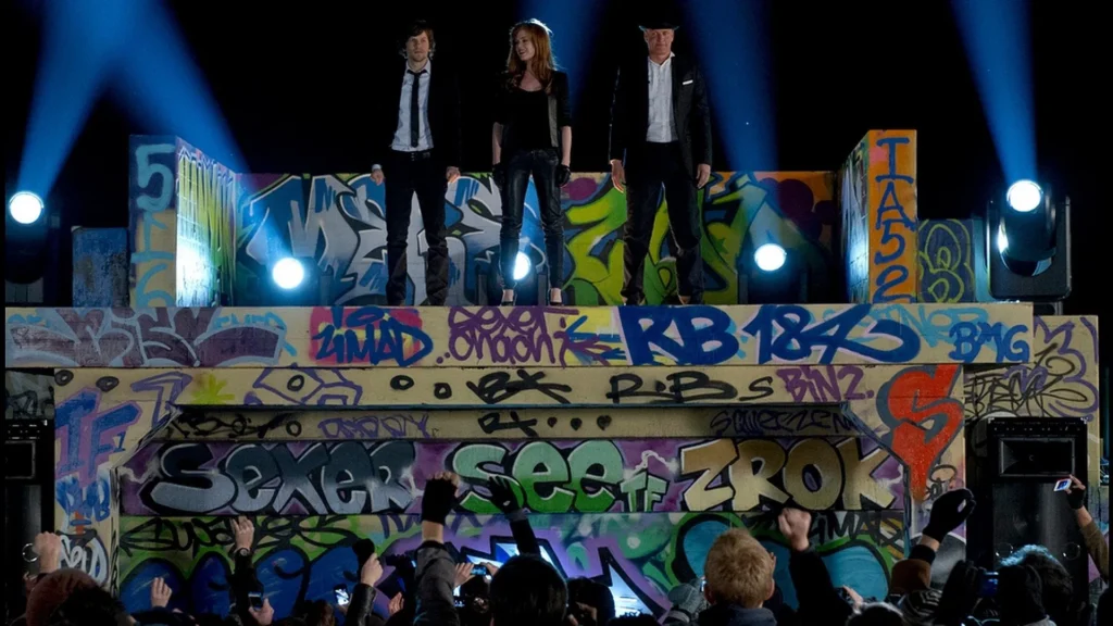 Movie Still from Now You See Me. This is the "final" trick that the Horsemen had planned. -The Horsemen stand on top of a platform while being surrounded by a massive crowd and being on the run from the feds.