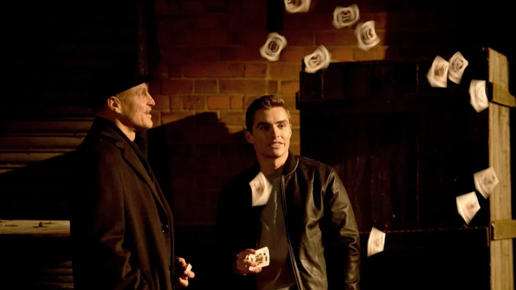 Merritt McKinney (Woody Harrelson) in a hat and Jack Wilder (Dave Franco) smiling,  doing card tricks from a beginning scene in Now You See Me 2.