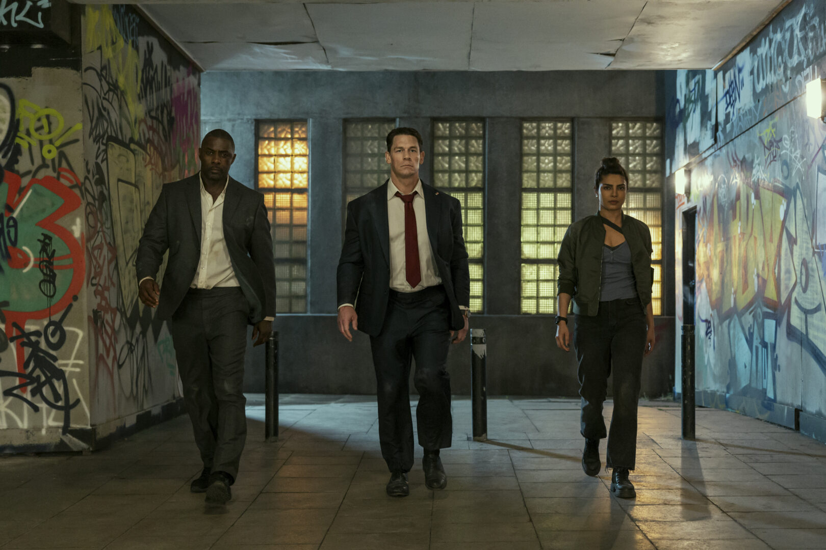 Idris Elba, John Cena, and Priyanka Chopra Jonas walking confidently through a graffiti-covered tunnel in Heads of State.